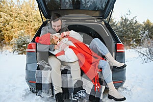 Happy couple sitting in open car back, having stop off. Romantic traveling concept. Winter forest