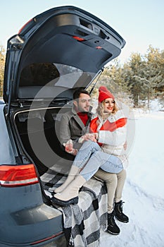 Happy couple sitting in open car back, having stop off. Romantic traveling concept. Winter forest