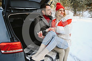 Happy couple sitting in open car back, having stop off. Romantic traveling concept. Winter forest