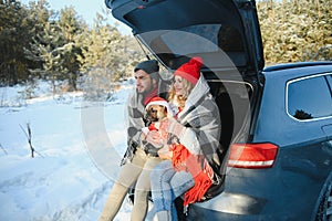 Happy couple sitting in open car back, having stop off. Romantic traveling concept. Winter forest