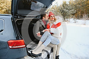 Happy couple sitting in open car back, having stop off. Romantic traveling concept. Winter forest