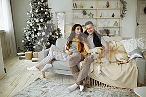 Happy couple is sitting on sofa with dog, christmas. new year at home. family and date