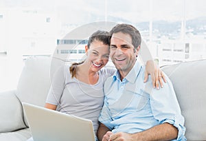 Happy couple sitting on the sofa using laptop together