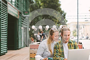 Happy couple sitting in street cafe together and using laptop