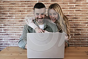 Happy couple sitting and working together from home with a laptop. Young adult man and woman using computer online in