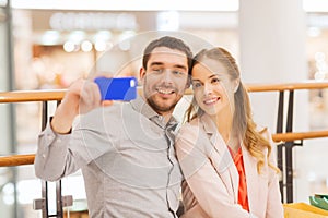 Happy couple with smartphone taking selfie in mall