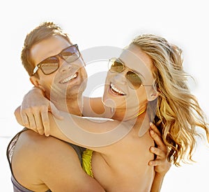 Happy, couple and smile with hug by beach with sunglasses, vacation and holiday for memories or honeymoon. Woman, man