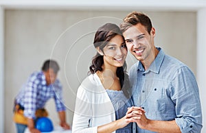 Happy couple smiling with architect in background. Portrait of young loving couple smiling holding hands with architect