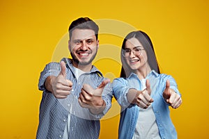 Happy couple smiling and showing thumbs up over yellow background