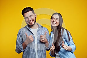 Happy couple smiling and showing thumbs up over yellow background