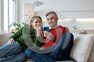 Happy couple spending lazy weekends together at home, surfing in mobile internet, shopping online