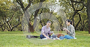 Happy couple spending time together drinking hot tea from a thermos and eating croissants on a picnic in a green garden