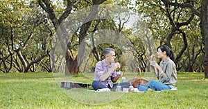 Happy couple spending time together drinking hot tea from a thermos and eating croissants on a picnic in a green garden