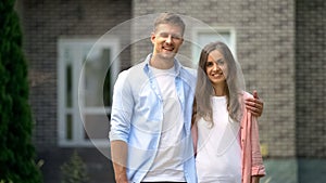 Happy couple standing against new bought house, real estate agency advertisement