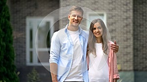 Happy couple standing against new bought house, real estate agency advertisement photo