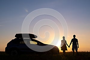 Happy couple standing near their car at sunset. Young man and woman enjoying time together travelling by vehicle