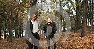 Happy couple stands distantly, they pose and smile in autumn sunny park