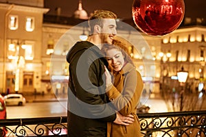 A happy couple stands in an embrace on the street in the evening in the festive lights