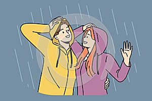 Happy couple stands in rain in hoods and hugs rejoicing at cloudy weather and autumn downpour