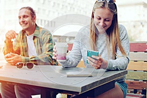 Happy couple in street cafe together, smiling woman using mobile phone, outdoors