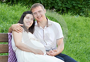 Happy couple in summer city park outdoor, pregnant woman, bright sunny day and green grass, beautiful people portrait