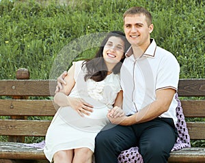 Happy couple in summer city park outdoor, pregnant woman, bright sunny day and green grass, beautiful people portrait, yellow tone