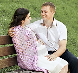 Happy couple in summer city park outdoor, pregnant woman, bright sunny day and green grass, beautiful people portrait, yellow tone