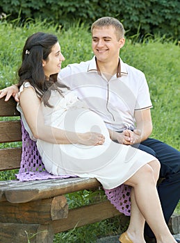 Happy couple in summer city park outdoor, pregnant woman, bright sunny day and green grass, beautiful people portrait, yellow tone