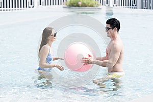 Happy couple and summer vacations at resort. Male and female playing in the pool with a beach ball