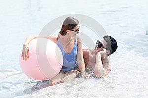 Happy couple and summer vacations at resort. Male and female playing in the pool with a beach ball