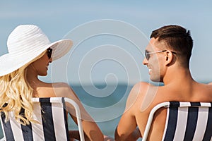 Happy couple sunbathing in chairs on summer beach