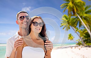 Happy couple in sunglasses over tropical beach