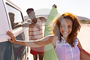 Happy couple with surfboard leaning on camper van at beach