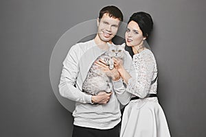 Happy couple sweetheart with cute cat posing over grey background. Valentine& x27;s day concept advertising