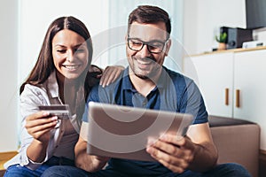 Happy couple with tablet pc computer and credit or bank card shopping online at home