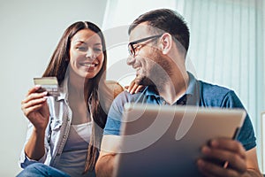 Happy couple with tablet pc computer and credit or bank card shopping online at home