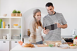 Happy couple with tablet pc cooking food at home