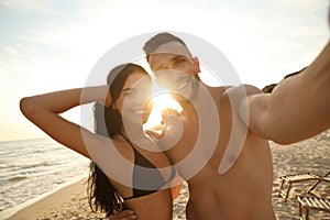 Happy couple taking selfie on beach at sunset