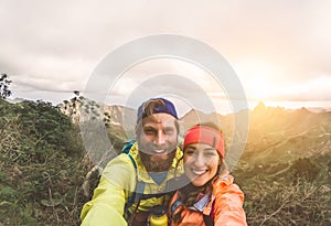 Happy couple taking selfie while doing trekking excursion on mountains - Young hikers having fun on exploration nature tour