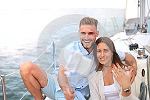 Happy couple taking a selfie after engagement proposal at sailing boat, relaxing on a yacht at the sea.