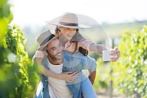 Happy couple taking selfie while piggybacking at vineyard