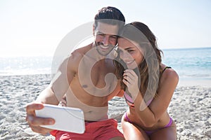 Happy couple taking selfie while sitting at beach photo