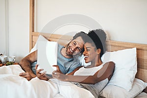 Happy couple taking selfie on a tablet in bed together after waking up. Interracial husband and wife enjoying their