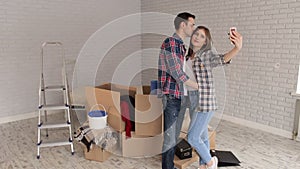 Happy couple taking a selfie in their new apartment, a happy man kisses his wife