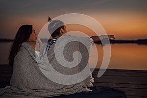Happy couple of teens enjoying in romantic date while sitting covered with blanket during sunset