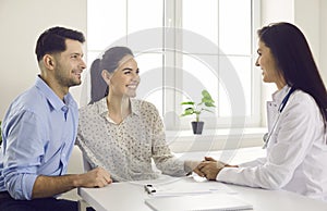 Happy couple and their family doctor sitting at table, holding hands and smiling
