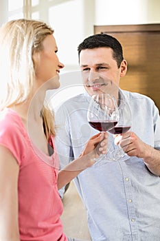 Happy couple toasting red wine glasses in kitchen