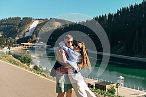 Happy couple of tourists having fun on a walk in a mountain resort on a sunny summer day against the backdrop of mountains and