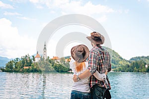 Happy couple of tourists in love standing back view. on the background Bled Lake and Church on the Island, Slovenia. Summer time