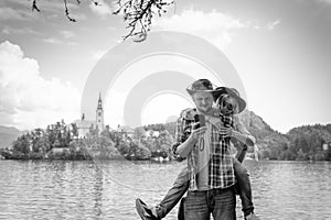 Happy couple of tourists in love standing on a wooden pier on the background with Bled Lake and Church on the Island, Slovenia.